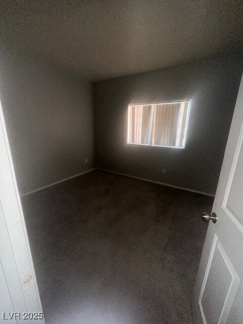 Spare room with dark carpet and baseboards