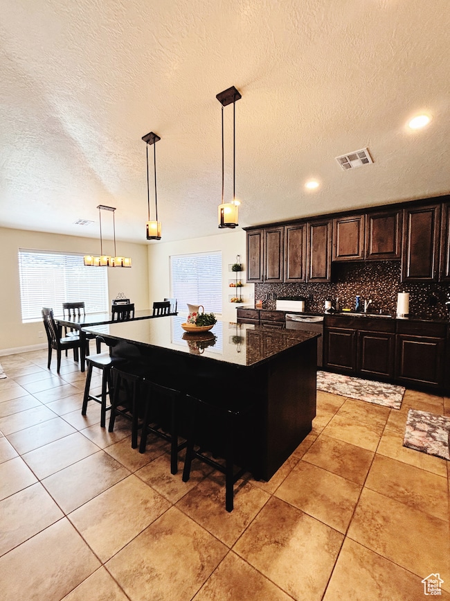 Kitchen with backsplash, a textured ceiling, a kitchen breakfast bar, hanging light fixtures, and a kitchen island