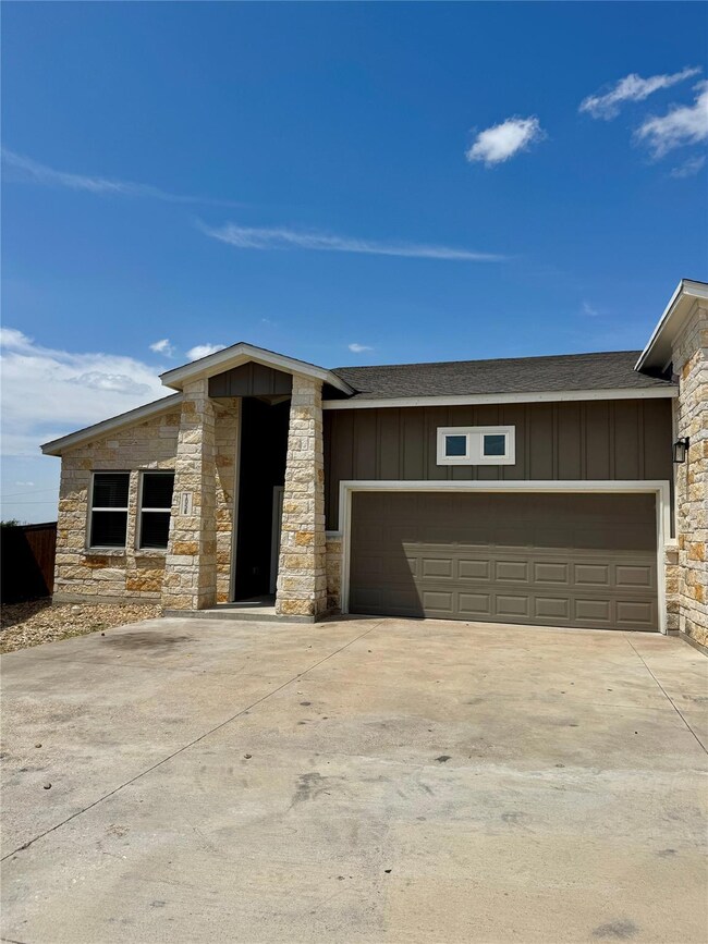 View of front facade featuring roof with shingles, board and batten siding, stone siding, and driveway
