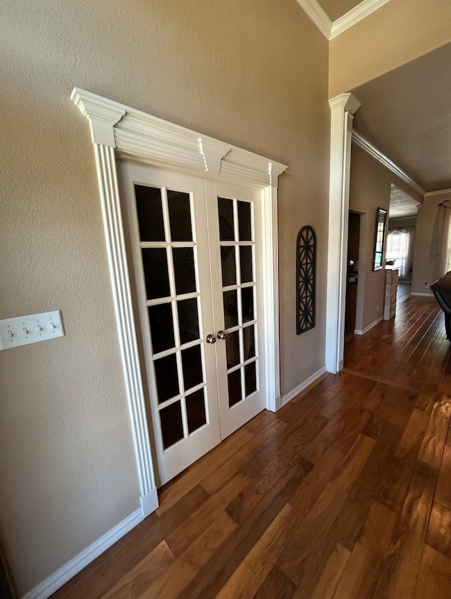 Corridor featuring french doors, dark wood-style floors, crown molding, a textured wall, and decorative columns