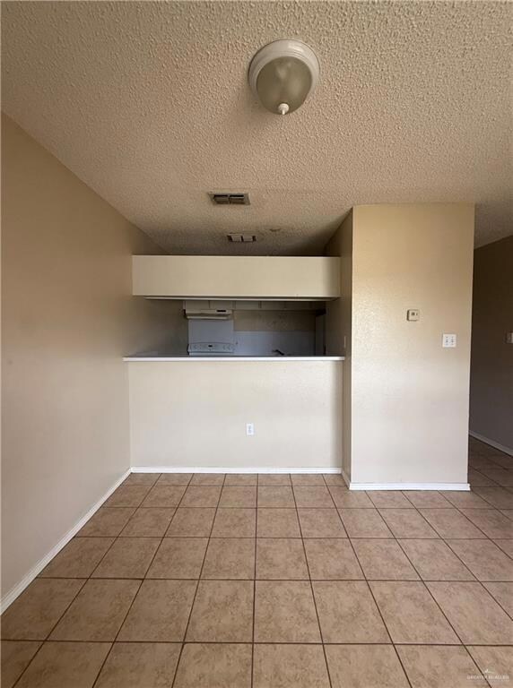 Tiled spare room featuring a textured ceiling and baseboards