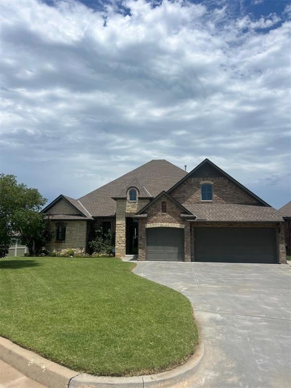 View of front of property with driveway, a front lawn, an attached garage, roof with shingles, and stone siding