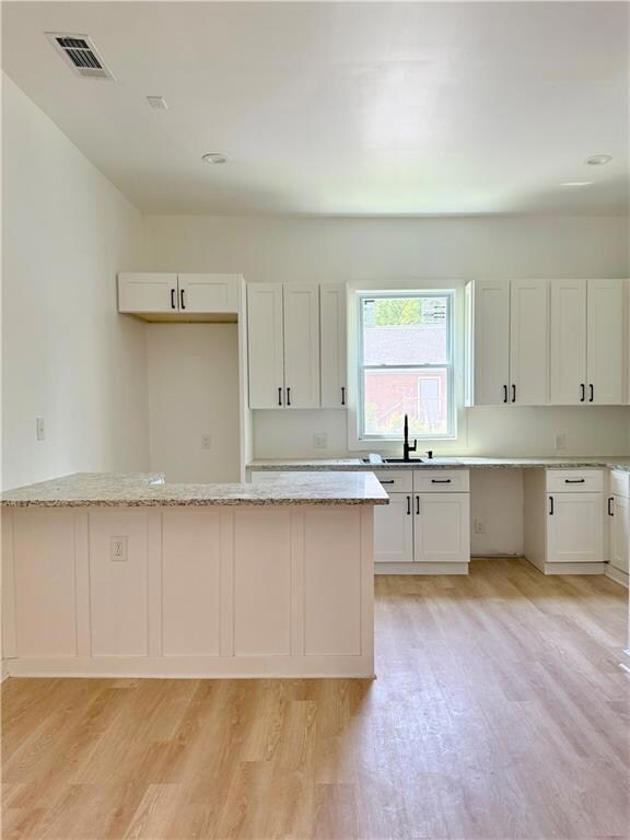 Kitchen with visible vents, a sink, light stone counters, white cabinets, and light wood-style flooring