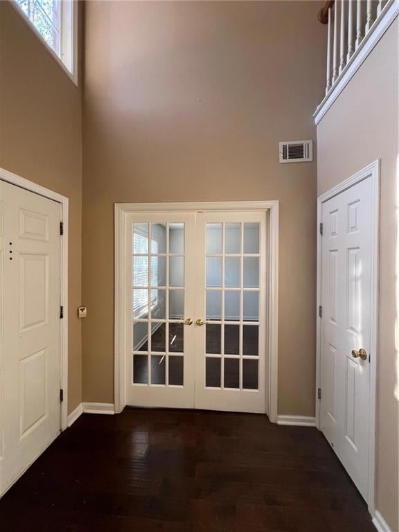 Entrance foyer featuring healthy amount of natural light, french doors, a towering ceiling, and dark wood-type flooring