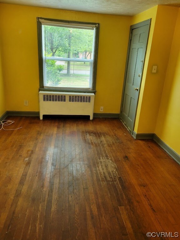 Unfurnished bedroom with radiator, a textured ceiling, and dark hardwood / wood-style floors