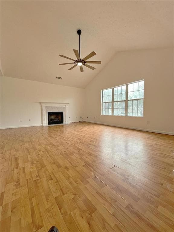 Unfurnished living room with ceiling fan, light wood-style flooring, lofted ceiling, a premium fireplace, and baseboards