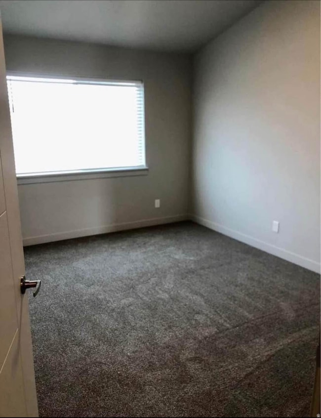 Spare room featuring dark colored carpet and baseboards