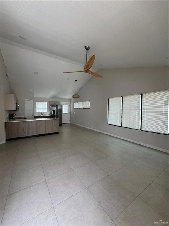 Unfurnished living room featuring a sink, vaulted ceiling, baseboards, a ceiling fan, and light tile patterned floors