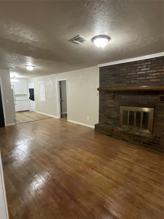 Unfurnished living room featuring wood-type flooring, brick wall, a fireplace, and a textured ceiling