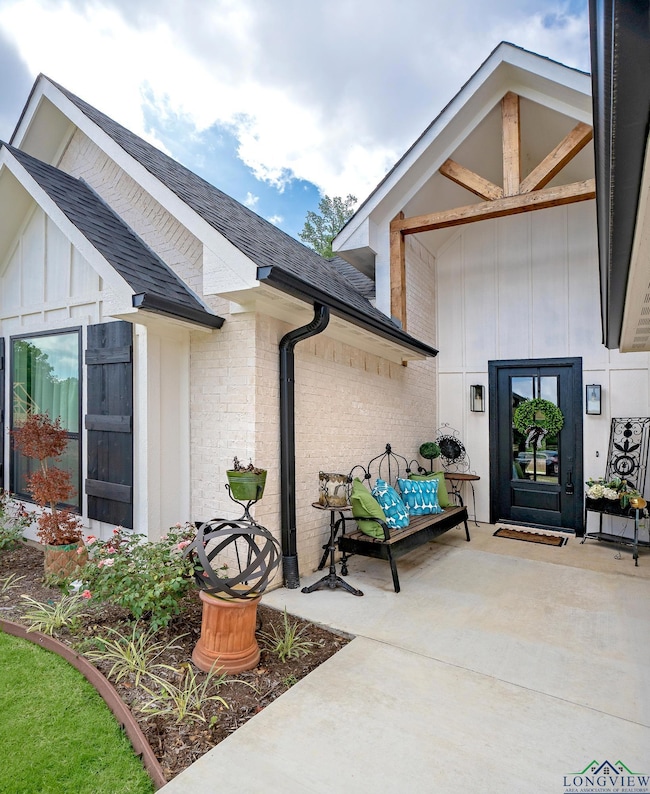 Entrance to property with a shingled roof, brick siding, a patio area, and board and batten siding