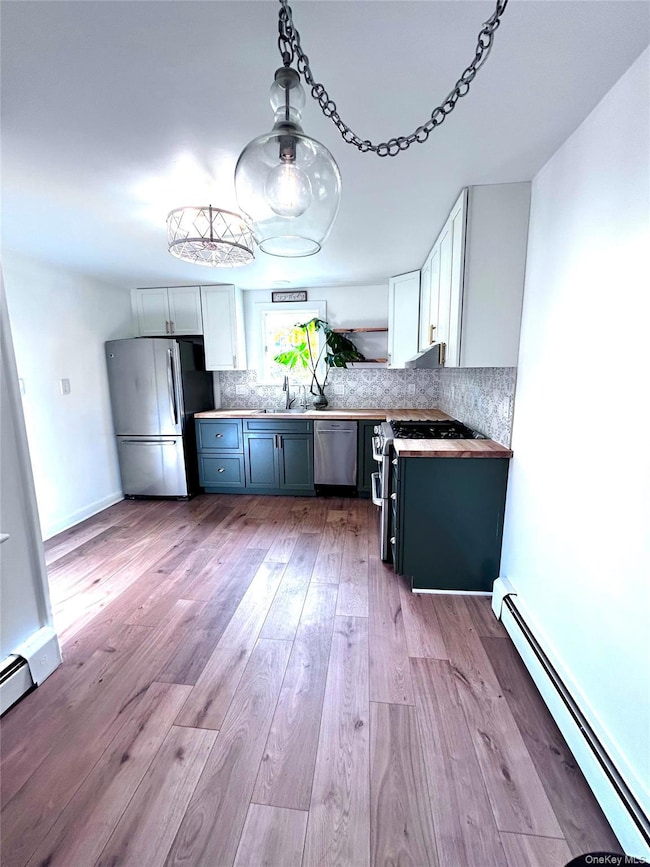 Kitchen with a baseboard radiator, white cabinets, appliances with stainless steel finishes, and light wood-style flooring