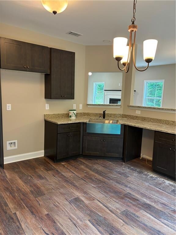 Kitchen with dark wood-style floors, dark brown cabinets, light stone countertops, hanging light fixtures, and a chandelier