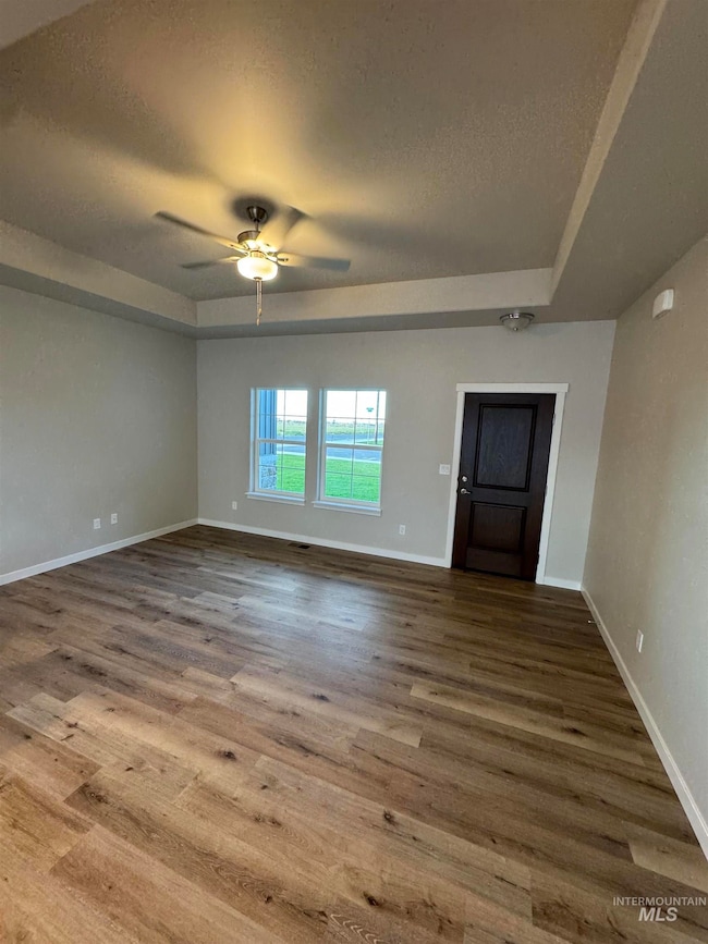 Empty room with a textured ceiling, wood finished floors, ceiling fan, and a raised ceiling
