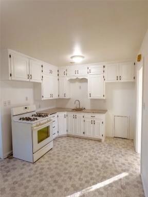 Kitchen with white gas range oven, light carpet, white cabinetry, and sink