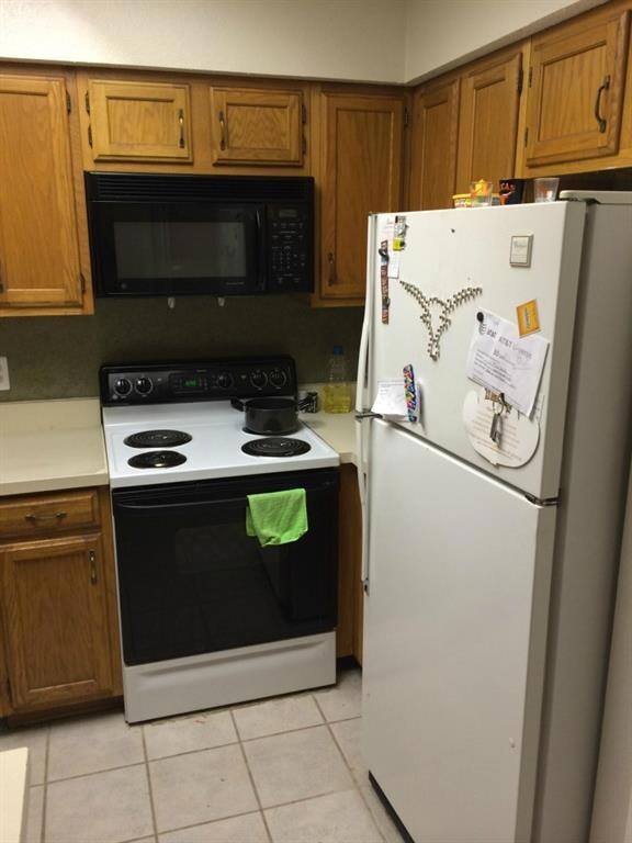 Kitchen featuring range with electric cooktop, freestanding refrigerator, brown cabinetry, black microwave, and light countertops