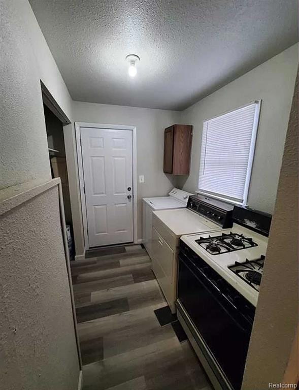 Kitchen featuring white gas range oven, a textured ceiling, washing machine and dryer, a textured wall, and light countertops