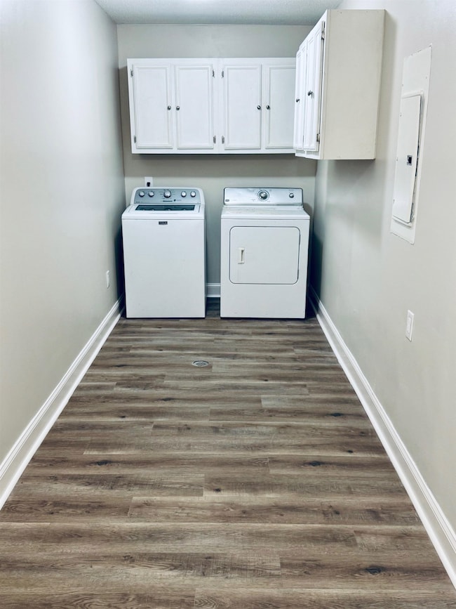 Laundry room featuring washer and dryer, cabinet space, dark wood-type flooring, and electric panel