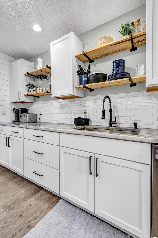 Kitchen featuring open shelves, a textured ceiling, light wood finished floors, light stone countertops, and recessed lighting