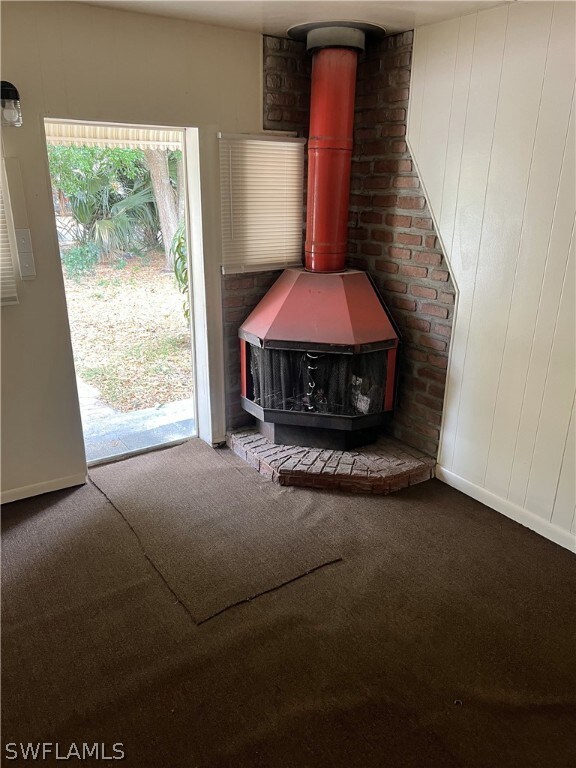 Unfurnished living room featuring carpet flooring and a wood stove