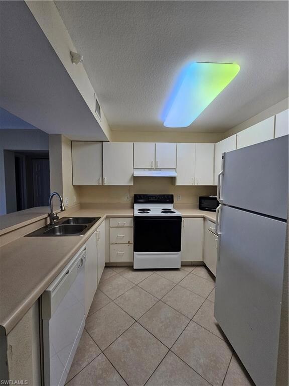 Kitchen with white appliances, a sink, under cabinet range hood, and light tile patterned floors