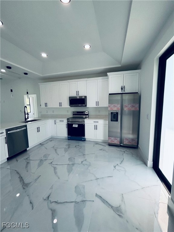 Kitchen with white cabinetry, a tray ceiling, appliances with stainless steel finishes, light marble finish flooring, and recessed lighting