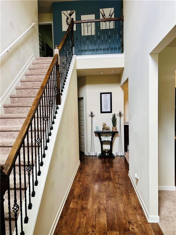 Staircase with wood finished floors, a towering ceiling, and baseboards