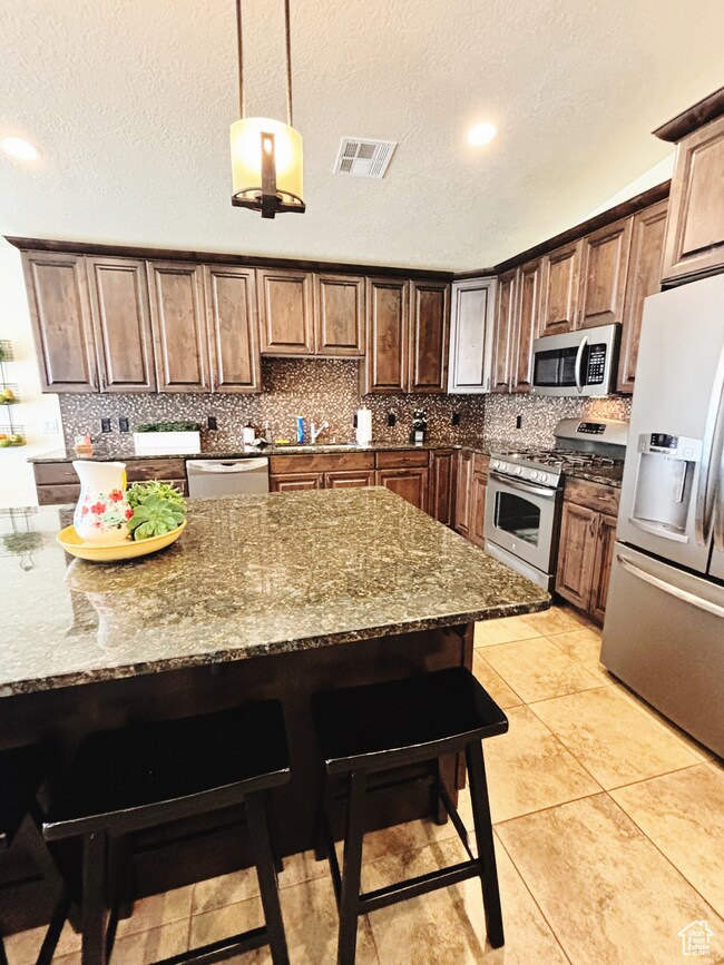 Kitchen featuring appliances with stainless steel finishes, a kitchen breakfast bar, tasteful backsplash, stone counters, and a textured ceiling