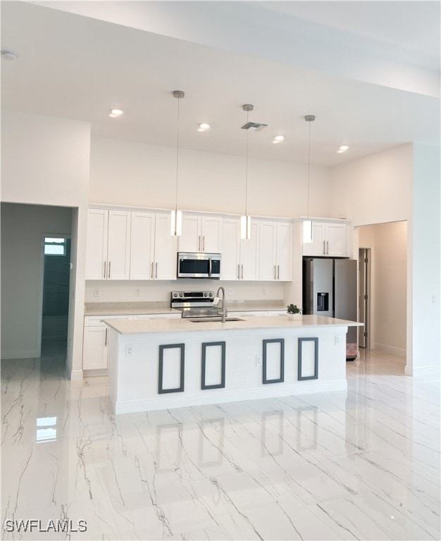 Kitchen with appliances with stainless steel finishes, a sink, a large island with sink, white cabinets, and a high ceiling