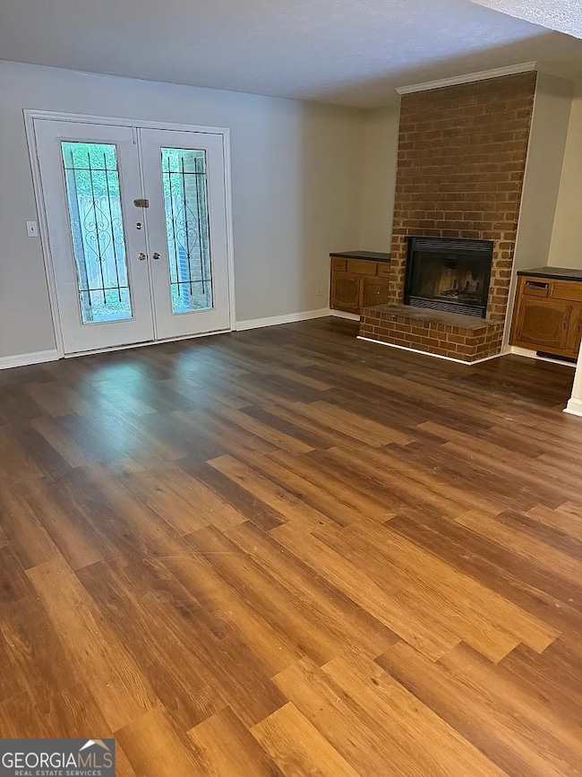 Spacious living room featuring rich flooring, a cozy brick fireplace, and French doors leading to the private patio.