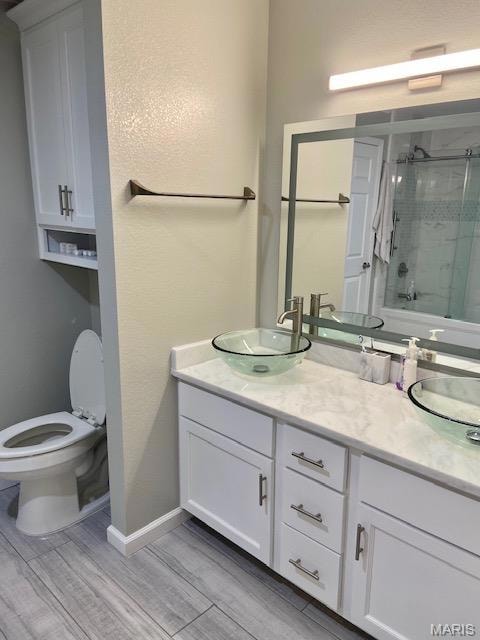 Bathroom with double vanity, enclosed tub / shower combo, light wood finished floors, and a textured wall
