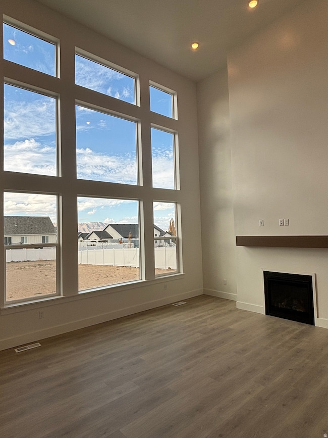 Unfurnished living room with a fireplace, dark wood-style flooring, a towering ceiling, recessed lighting, and a residential view