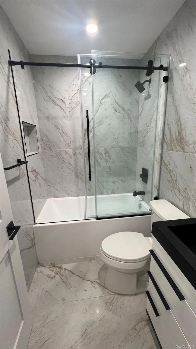 Bathroom with combined bath / shower with glass door, tile walls, marble finish flooring, and vanity