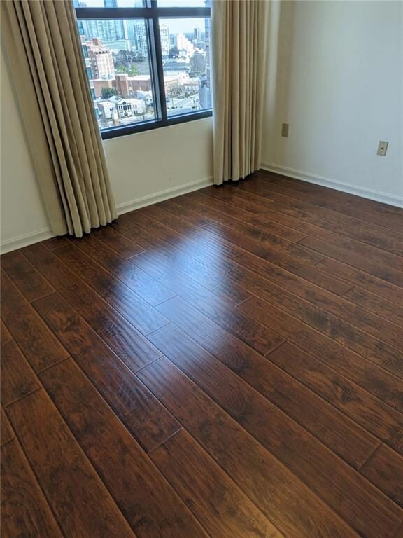 Unfurnished room featuring baseboards and dark woo