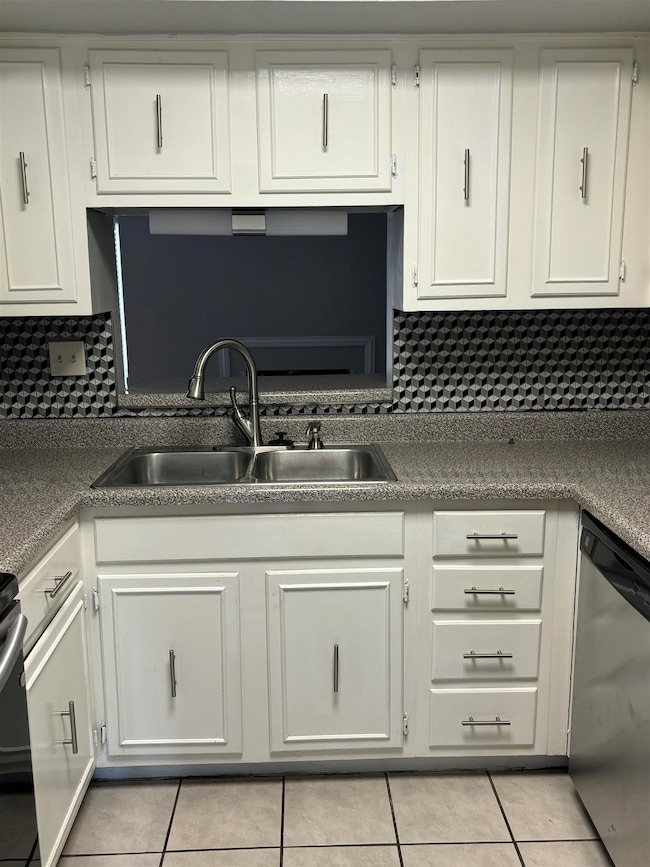 Kitchen featuring stainless steel dishwasher, a sink, light tile patterned floors, and white cabinetry