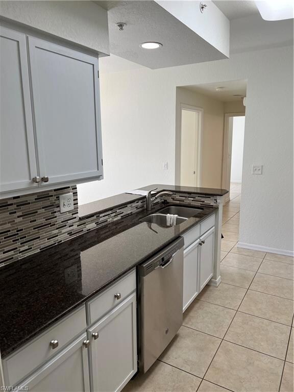 Kitchen featuring stone counters, dishwasher, light tile patterned flooring, white cabinets, and a textured wall