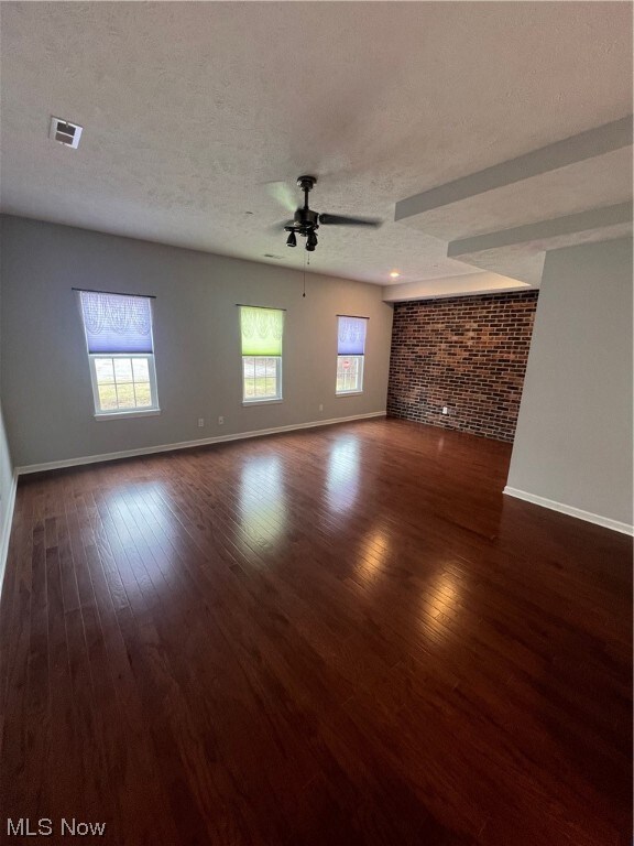 Unfurnished living room with brick wall, dark hardwood / wood-style flooring, ceiling fan, and a textured ceiling