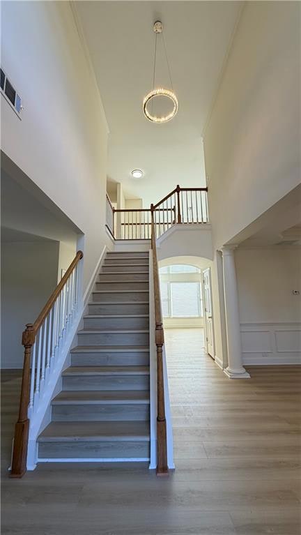 Stairway with a high ceiling, wood finished floors, decorative columns, crown molding, and a chandelier
