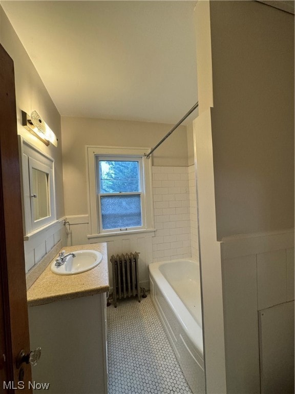 Bathroom with radiator, tile floors, tiled shower / bath combo, and large vanity