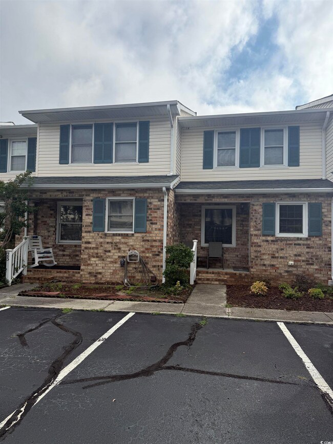 Townhome / multi-family property with a porch, uncovered parking, and brick siding