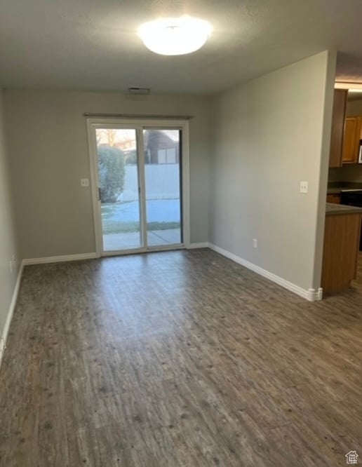 Spare room with dark wood-type flooring and baseboards