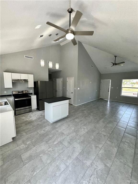 Kitchen with white cabinets, high vaulted ceiling, stainless steel appliances, light tile floors, and ceiling fan