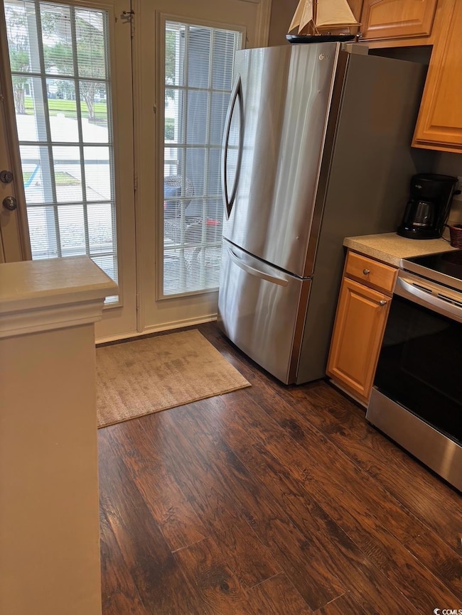 Kitchen with stainless steel appliances, light countertops, dark wood-style flooring, and brown cabinetry