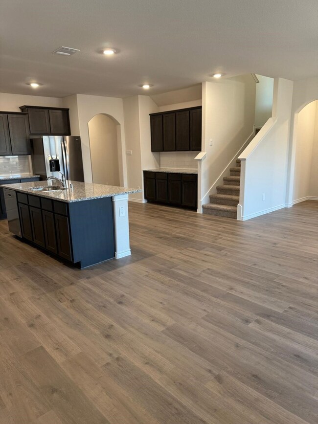 Kitchen featuring arched walkways, backsplash, light stone counters, stainless steel appliances, and dark wood-style flooring