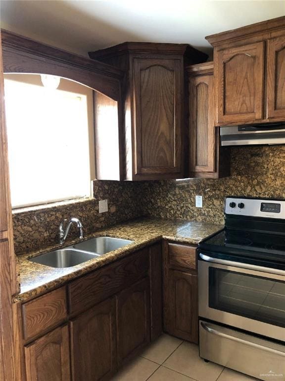Kitchen with stainless steel electric range oven, decorative backsplash, light tile patterned floors, and under cabinet range hood