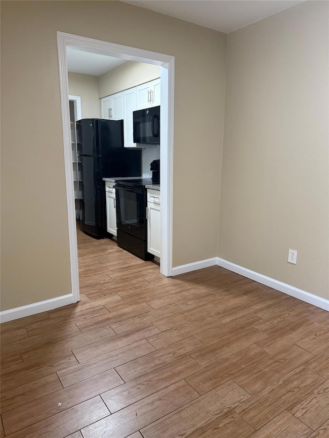 Kitchen featuring light wood-type flooring, white cabinetry, and black appliances