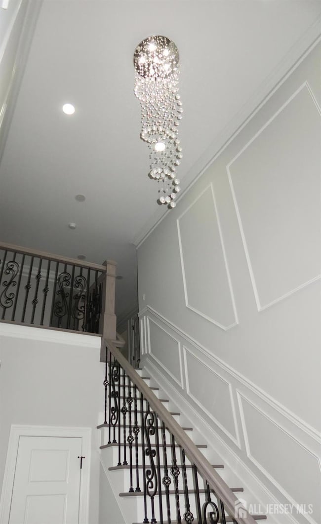 staircase featuring a decorative wall, crown molding, a chandelier, and recessed lighting