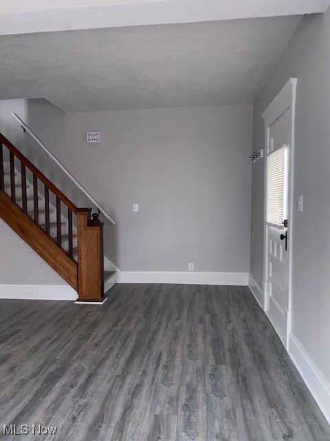 Unfurnished living room featuring dark wood-style floors and stairs