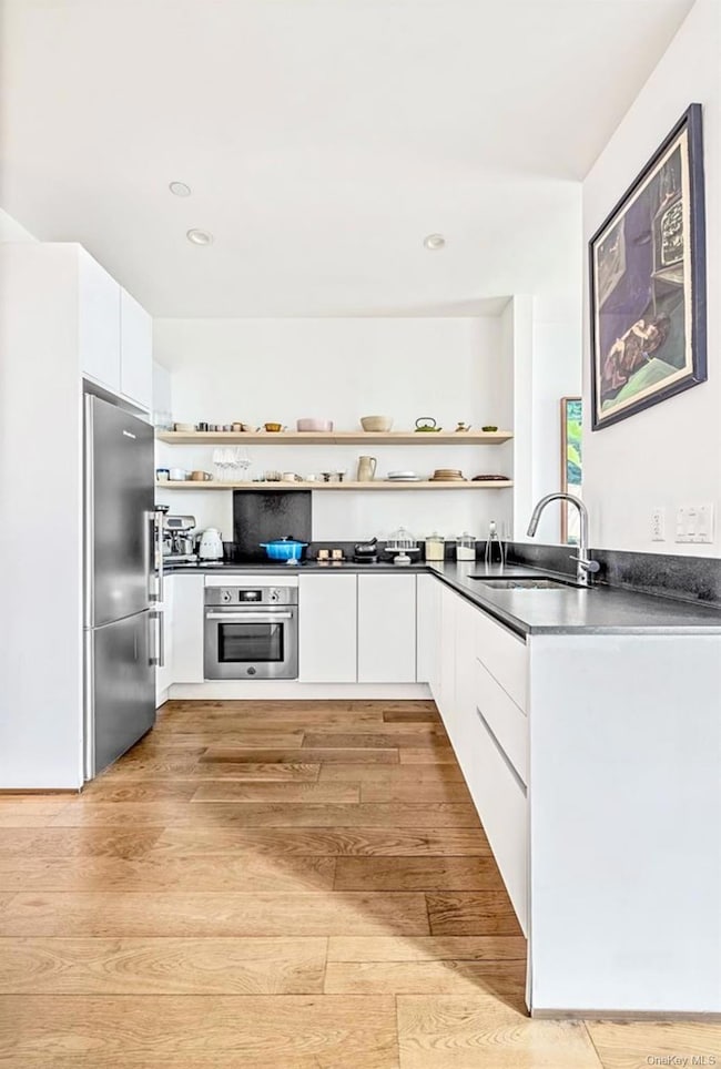 Kitchen featuring open shelves, light wood-style floors, white cabinetry, appliances with stainless steel finishes, and modern cabinets