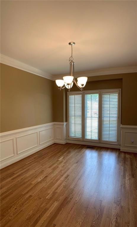 Unfurnished dining area with a chandelier, crown molding, wood finished floors, a wainscoted wall, and a decorative wall