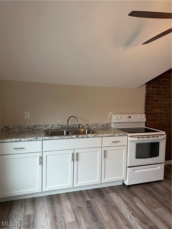 Kitchen featuring sink, white cabinetry, range, and lofted ceiling